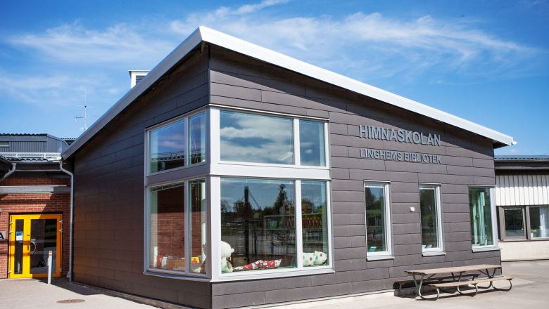 Utsidan av Himnaskolan där Linghems bibliotek ligger. Ett litet hus med mörkgrå fasad och stora fönster