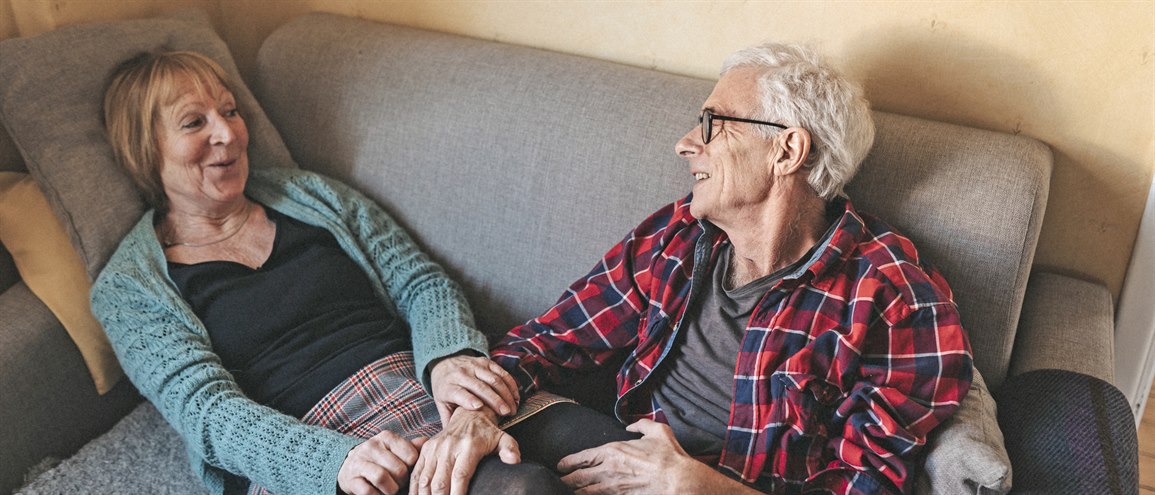 An older couple smiling and talking at home in their couch
