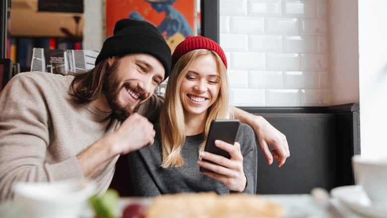 Yngre par som tittar på  en mobiltelefon på ett café.