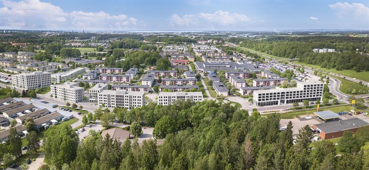 Flerbostadshus med 4-6 våningar omgivna av . I främre delen av bilden syns radhus och en bensinmack. I bakgrunden skymtar Linköpings innerstad med Domkyrkan och Roxen. 