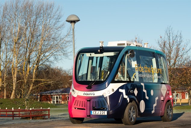 Foto på den självkörande bussen. Ett litet fordon som skiftar i färgerna rosa, lila, blått och vitt. Bussen har stora fönster med texten Ride the future. 