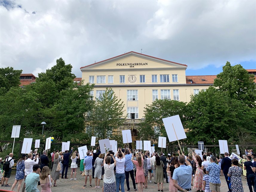 Studenter möter anhöriga som står med studentplakat utanför Folkungaskolan.