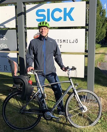 Man med cykel framför skyltar till göretaget Sick