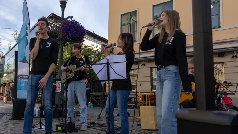 Fyra ungdomar spelar instrument och sjunger. De står utomhus på stora torget