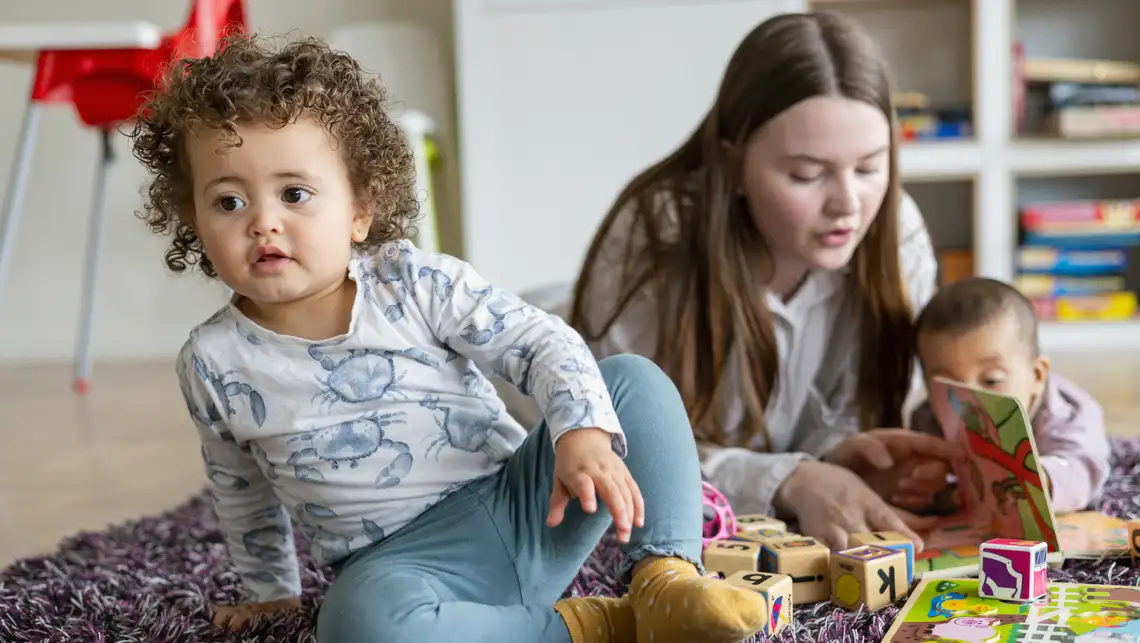 Litet barn sitter på en matta och leker.