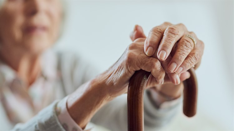 Äldre kvinna som håller sina händer på en käpp