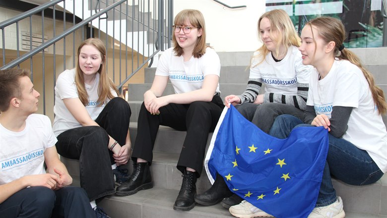 Elever sitter i en trappa och håller i EU-flagga